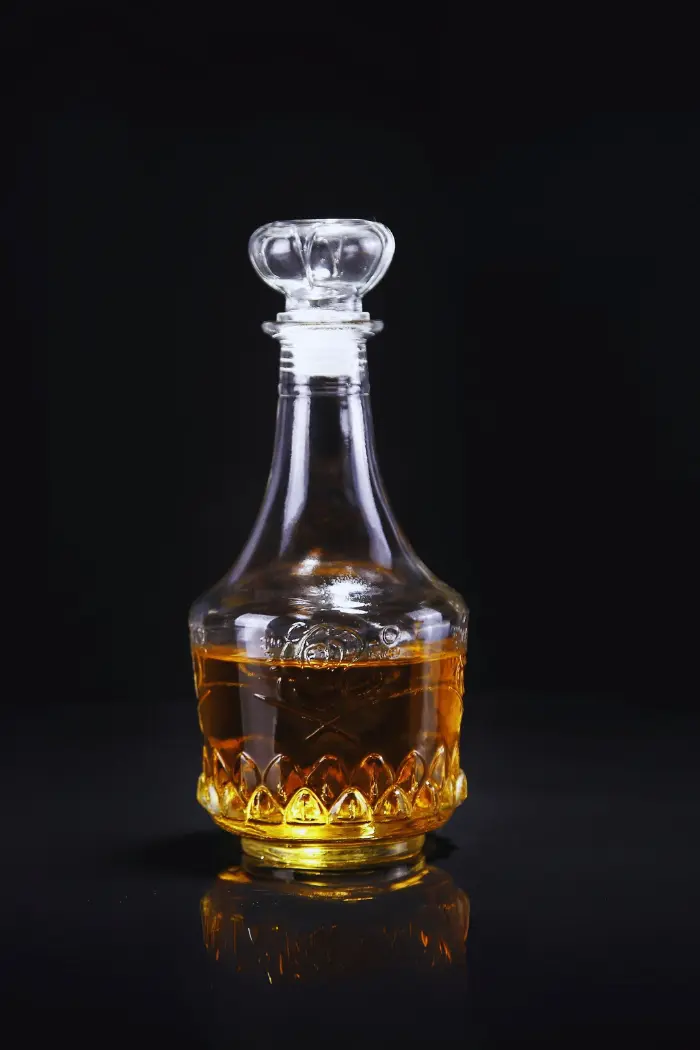 carafe à whisky gravée en verre, remplie de whisky, posée sur une table entourée de verres