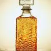 carafe à whisky carrée en verre transparent avec bouchon sculpté, posée sur une surface mouillée, remplie de whisky ambré