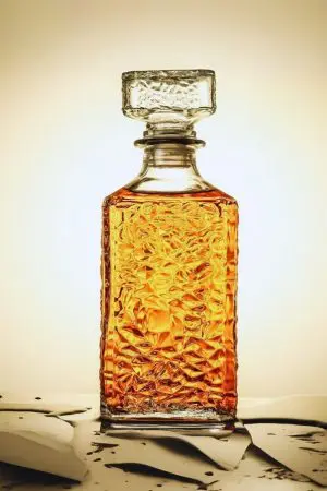 carafe à whisky carrée en verre transparent avec bouchon sculpté, posée sur une surface mouillée, remplie de whisky ambré