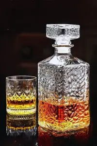 carafe à whisky carrée en verre tenue inclinée à la main, fond noir, remplie de whisky ambré