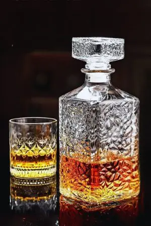 carafe à whisky carrée en verre tenue inclinée à la main, fond noir, remplie de whisky ambré