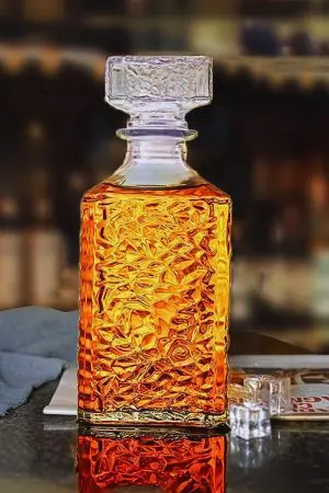 carafe à whisky carrée en verre et son verre assorti posés sur une surface mouillée, remplis de whisky ambré