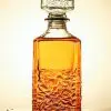 carafe à whisky carrée en verre transparent avec bouchon sculpté, posée sur une surface mouillée, remplie de whisky ambré