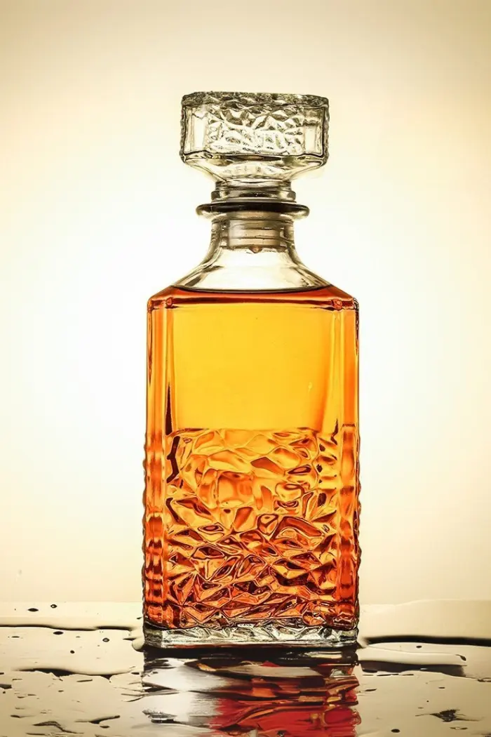 carafe à whisky carrée en verre transparent avec bouchon sculpté, posée sur une surface mouillée, remplie de whisky ambré
