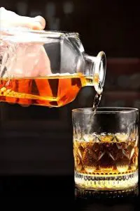 carafe à whisky carrée en verre transparent versant du whisky dans un verre bas assorti