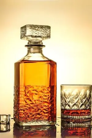 carafe à whisky carrée en verre et son verre assorti posés sur une surface mouillée, remplis de whisky ambré