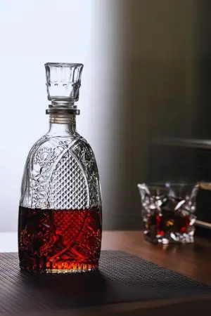 carafe à whisky vintage gravée, whisky foncé, posée sur table, verre à whisky flou en arrière-plan