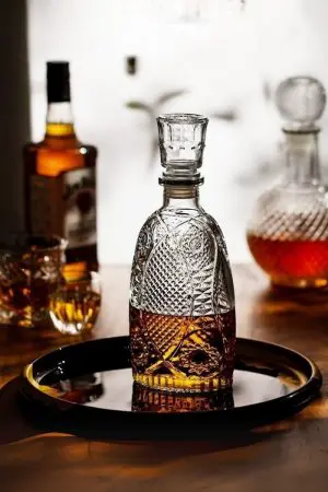carafe à whisky vintage sur plateau noir, verre gravé rempli de whisky, bouteilles en fond