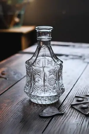 carafe à whisky hexagonale en verre gravé vide, posée sur table en bois