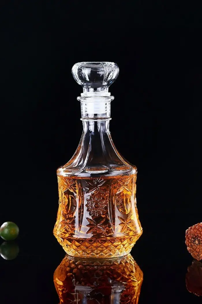 carafe à whisky hexagonale en verre gravé, remplie de whisky, posée sur table en bois