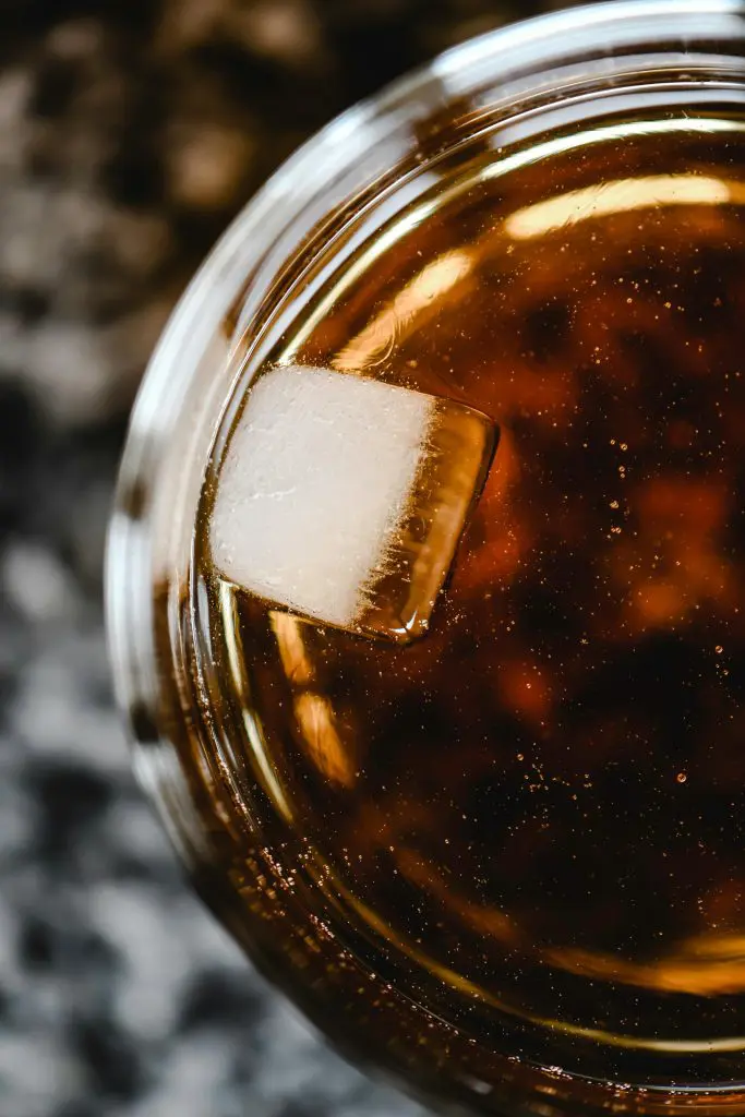 Gros plan d’un verre de whisky avec glaçon, mettant en valeur la couleur, la limpidité et la texture du spiritueux