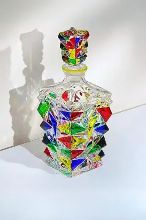 carafe italienne colorée pour whisky - décanteur vide en verre multicolore avec ombre sur mur blanc.