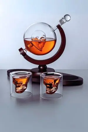 carafe à whisky globe crâne sur socle en bois et deux verres, fond clair