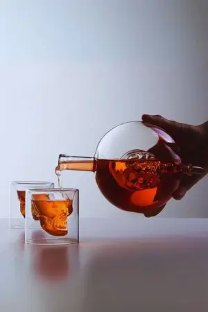 carafe à whisky globe crâne tenue et inclinée versant dans verre double paroi