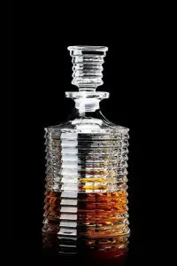 carafe à whisky en verre cannelé sur fond noir, partiellement remplie