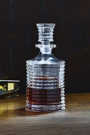 carafe à whisky en verre cannelé posée sur table en bois, fond sombre