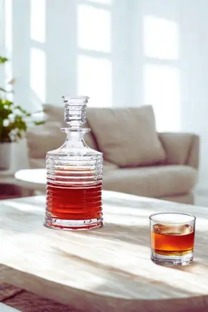 carafe à whisky en verre cannelé avec bouchon sur table en bois clair, verre tumbler à côté