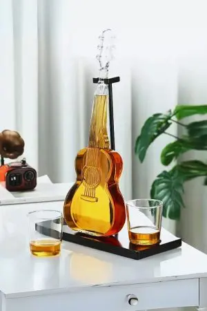 carafe guitare en verre sur socle noir avec deux verres partiellement remplis