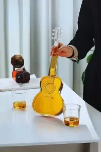 carafe guitare en verre remplie tenue par le manche sur table avec deux verres