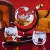 carafe globe en verre sur support bois avec deux verres gravés devant un fond rouge