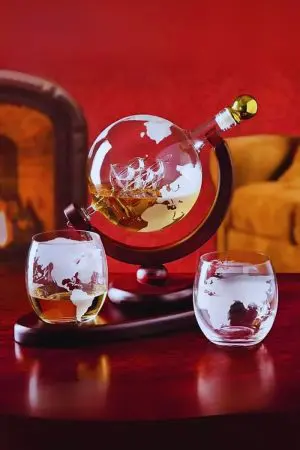 carafe globe en verre sur support bois avec deux verres gravés devant un fond rouge
