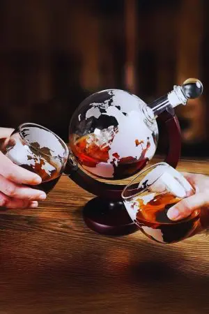 verres à whisky gravés monde portés à la main devant une carafe globe