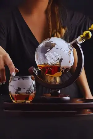 carafe globe en verre sur support bois et verre gravé posé à côté, scène sombre