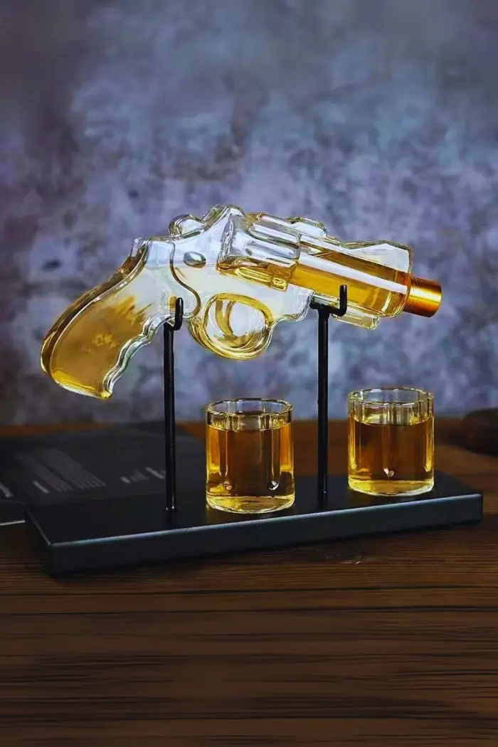 carafe à whisky revolver sur socle noir avec deux verres.