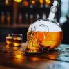 carafe à whisky tête de mort en verre inclinée avec bouchon, liquide ambré sur table