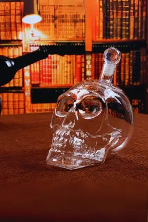 carafe à whisky tête de mort en verre debout avec bouchon facetté, fond bibliothèque