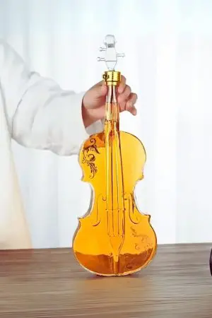 carafe à whisky violon en verre tenue à la main, remplie de liquide ambré, posée sur table en bois