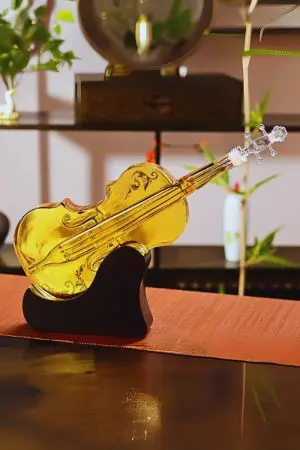 carafe à whisky violon posée sur socle en bois, liquide ambré, nappe orange