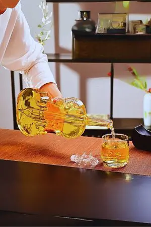 carafe à whisky violon versant un liquide ambré dans un verre tumbler sur table