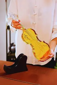 carafe à whisky violon en verre tenue à deux mains, liquide ambré, socle en bois posé sur la table