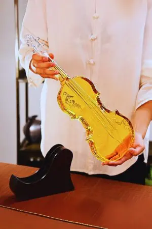 carafe à whisky violon en verre tenue à deux mains, liquide ambré, socle en bois posé sur la table