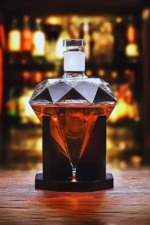carafe à whisky diamant en verre sur socle noir, liquide ambré, table en bois
