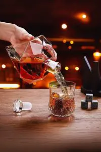 carafe à whisky diamant tenue et inclinée, verse un liquide ambré dans verre facetté