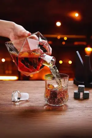 carafe à whisky diamant tenue et inclinée, verse un liquide ambré dans verre facetté