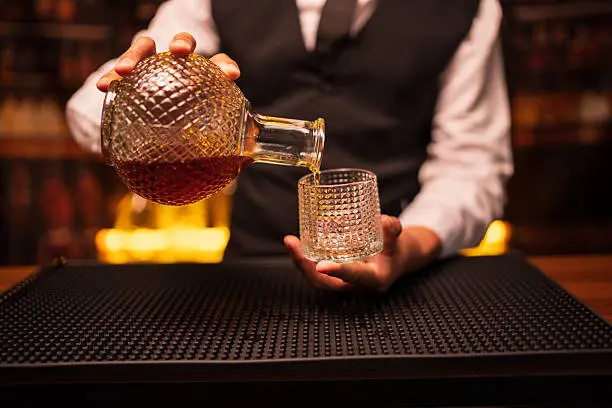barman versant du whisky ambré depuis une carafe ronde en cristal dans un verre taillé lors d’une dégustation