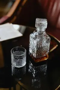 carafe à whisky en cristal à moitié remplie et verre vide sur une table noire brillante
