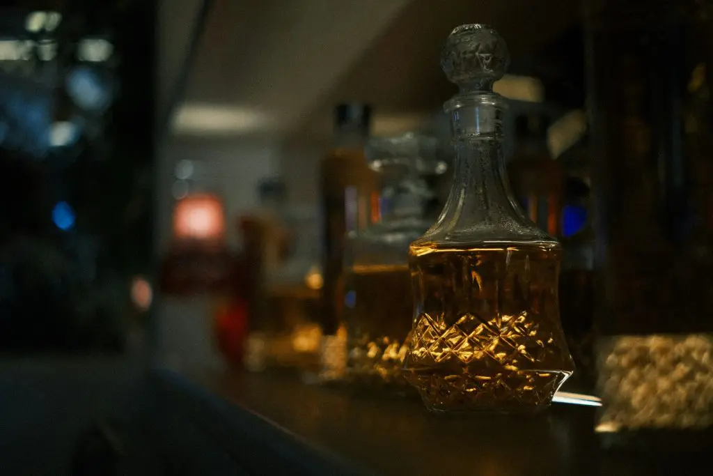 carafe à whisky en verre taillé posée sur une étagère dans une lumière tamisée, contenant un whisky ambré