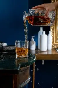 carafe à whisky en verre taillé versant le whisky dans un verre avec glaçons