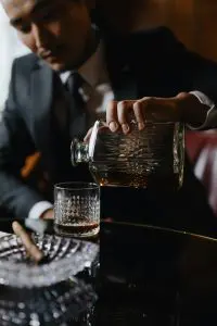 homme en costume servant du whisky avec une carafe en cristal dans un verre taillé