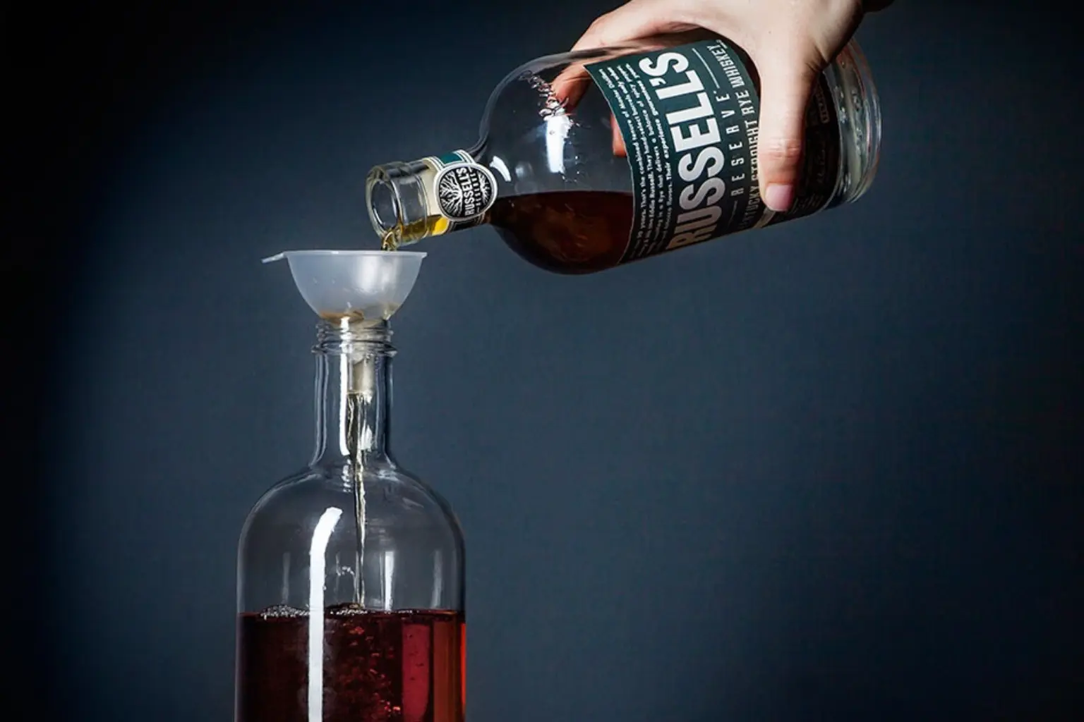 main versant du whisky depuis une bouteille d’origine dans une carafe à l’aide d’un petit entonnoir