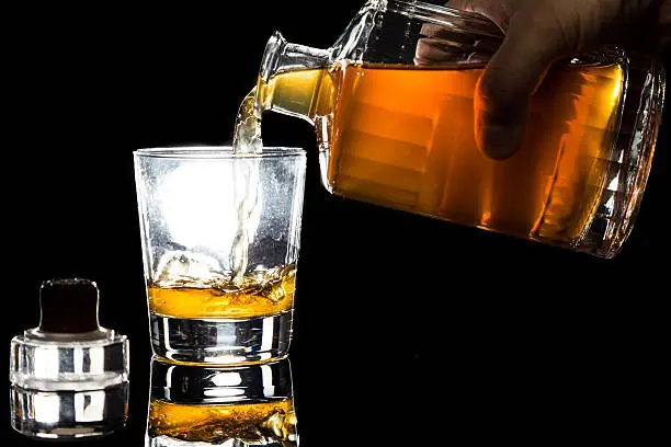 main versant du whisky ambré depuis une carafe en verre dans un verre transparent pour favoriser l’aération