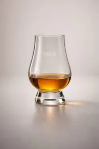 Verre Glencairn gravé avec initiales M&R, contenant du whisky, sur fond clair