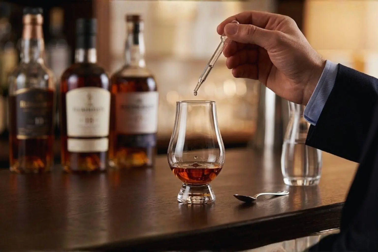 Gros plan d'une pipette déposant une goutte d'eau dans un verre de rhum ambré pour libérer les arômes.