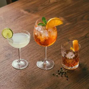 Trois verres de cocktails sur une table en bois représentant différents goûts : un Daiquiri acidulé, un Spritz doux et orangé, et un Old Fashioned ambré et sec.
