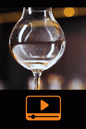 Verre à whisky tulipe en rotation sur fond sombre avec reflets lumineux dorés.