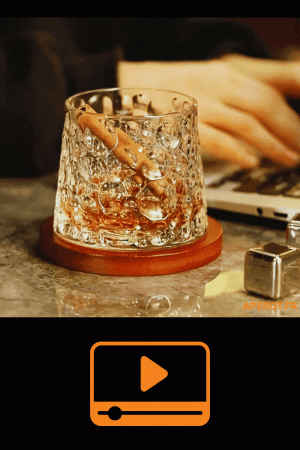 verre à whisky tumbler posé sur socle en bois avec boisson ambrée et glaçon en inox